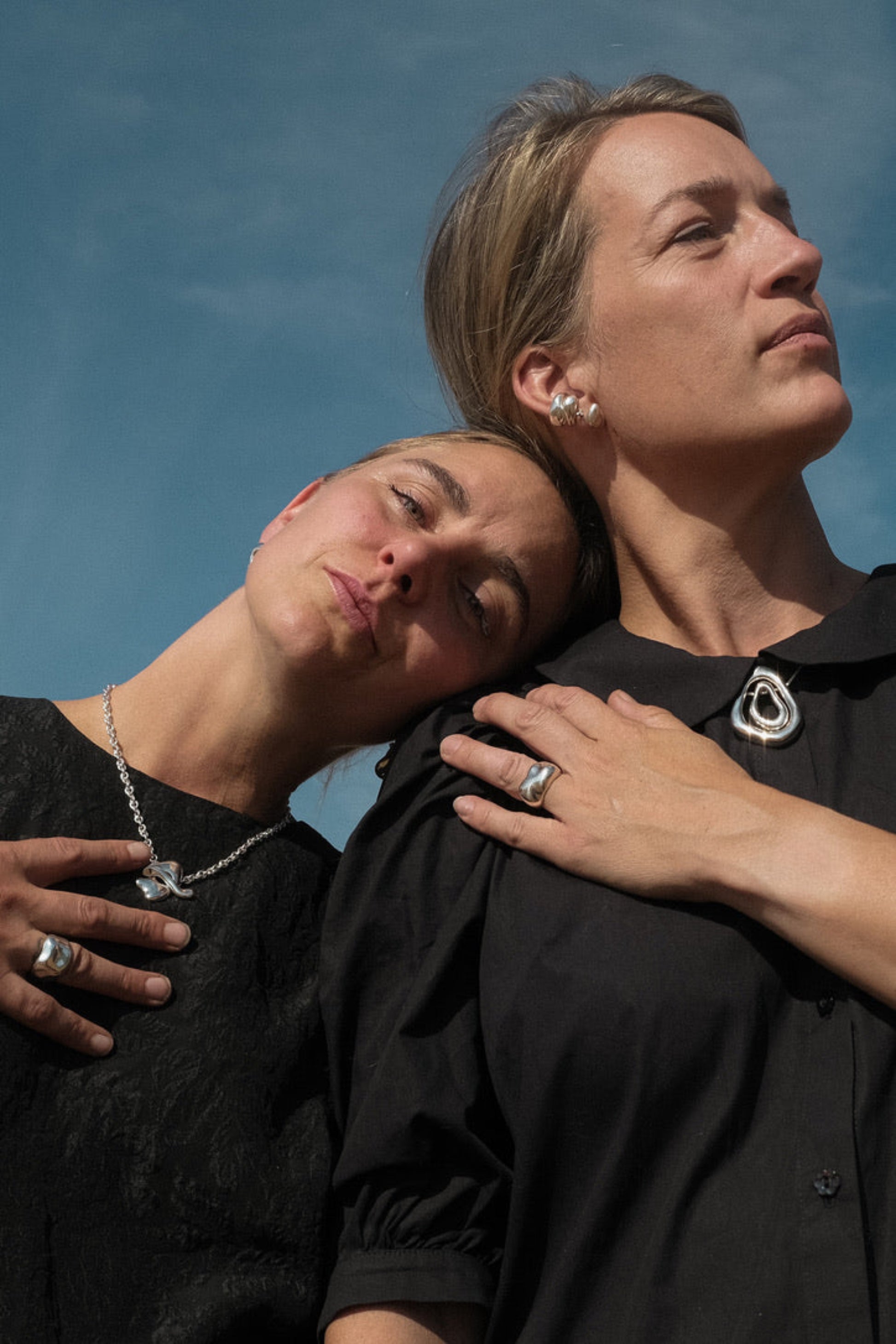 Two people wearing black shirts with jewelry against a blue sky.