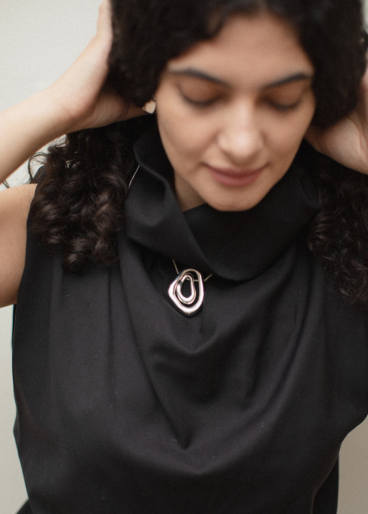 Close-up of the Andrea pendant, a sculptural contemporary design. The pendant is worn by a model in a black dress, showcasing its versatility as a statement piece when paired together or worn individually. The pendant contrasts beautifully against the dark outfit, adding a touch of light and elegance.