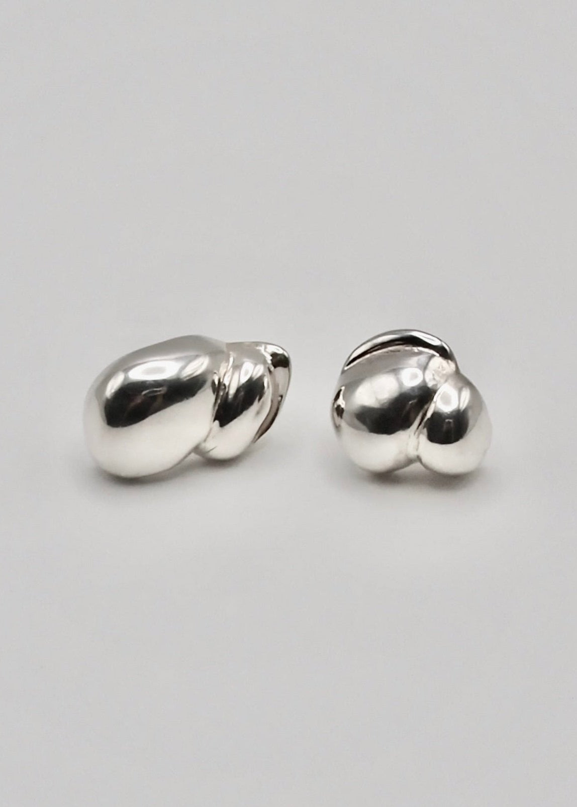 Camille Earrings displayed on a neutral background, highlighting their sculptural design and mirror-polished sterling silver finish. Each of them are different and representing the two parents. Minimalistic yet still a pair of statement earrings