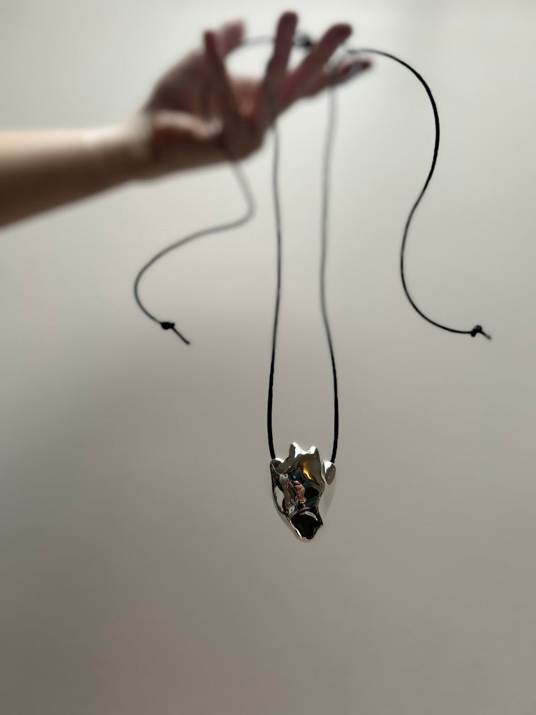 A hand holding the sculptured sterling silver heart hanging with a black cord