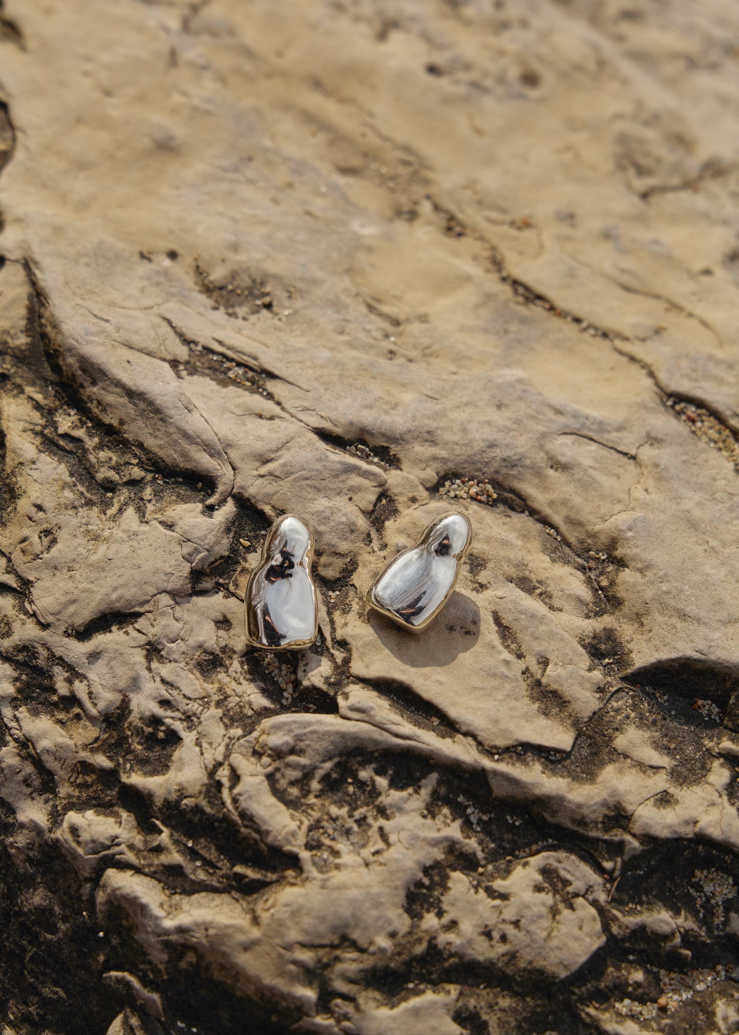 Detailed view of the Luna Earrings on the rocks in nature- focusing on their sleek design and the reflective quality of the 925 sterling silver.