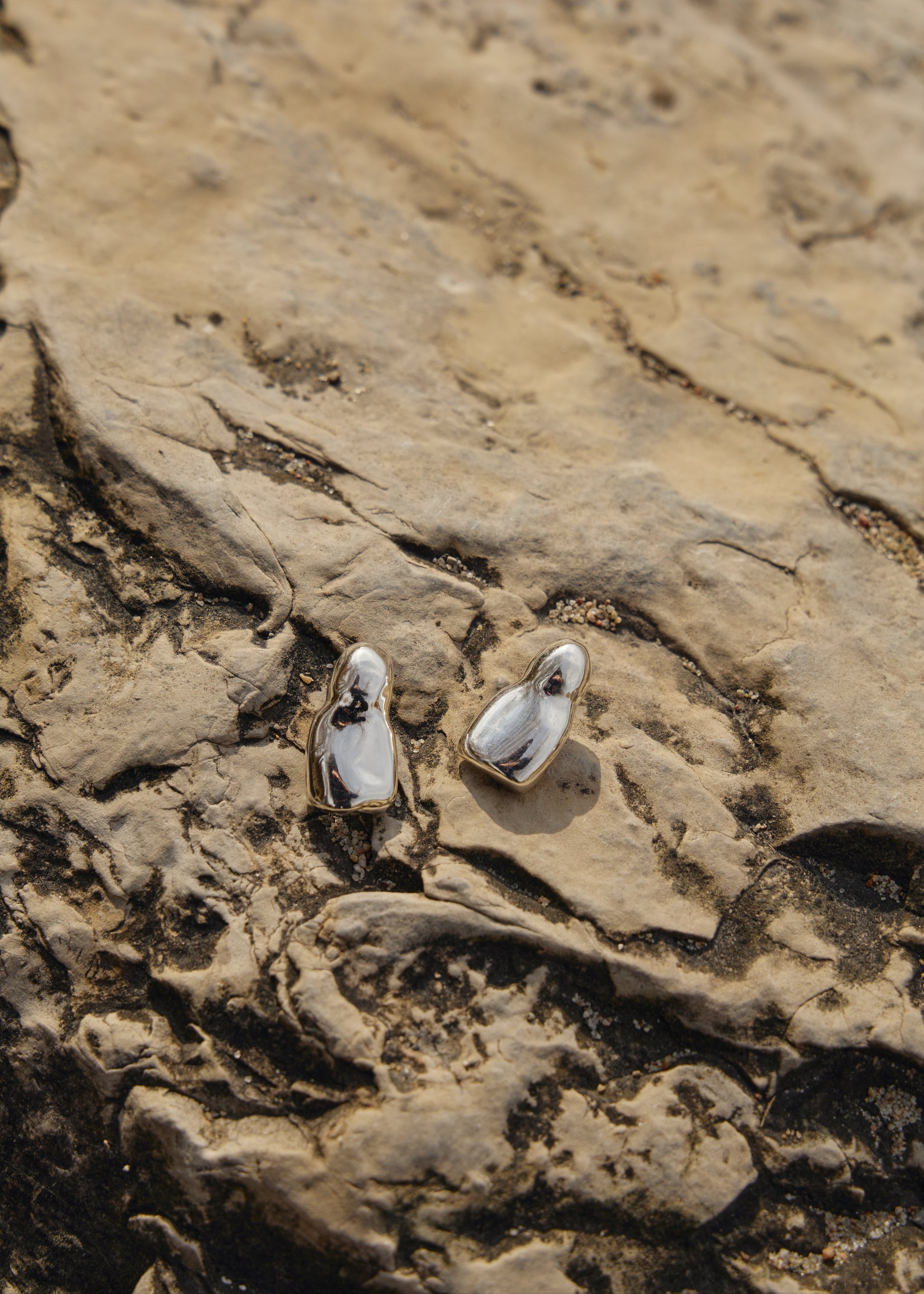 Detailed view of the Luna Earrings on the rocks in nature- focusing on their sleek design and the reflective quality of the 925 sterling silver.