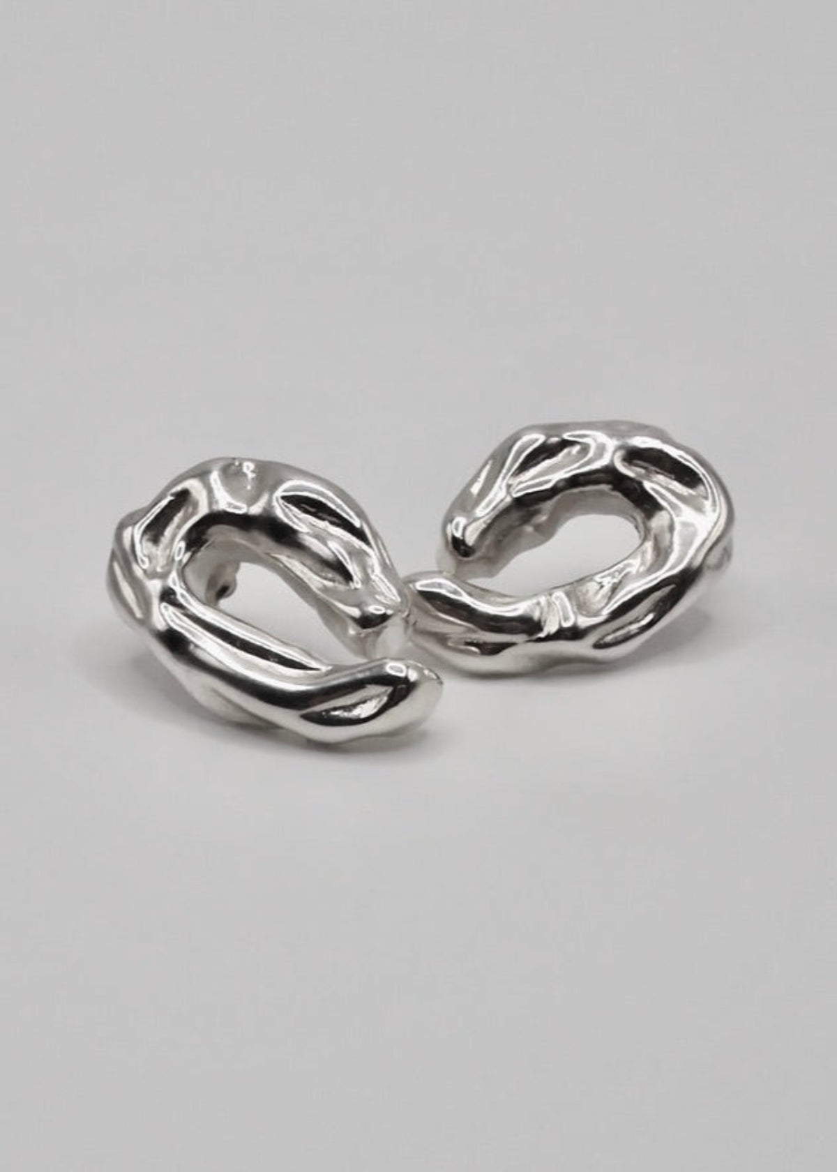 Ragna Earrings displayed on a neutral background, highlighting their sculptural design and mirror-polished sterling silver finish.