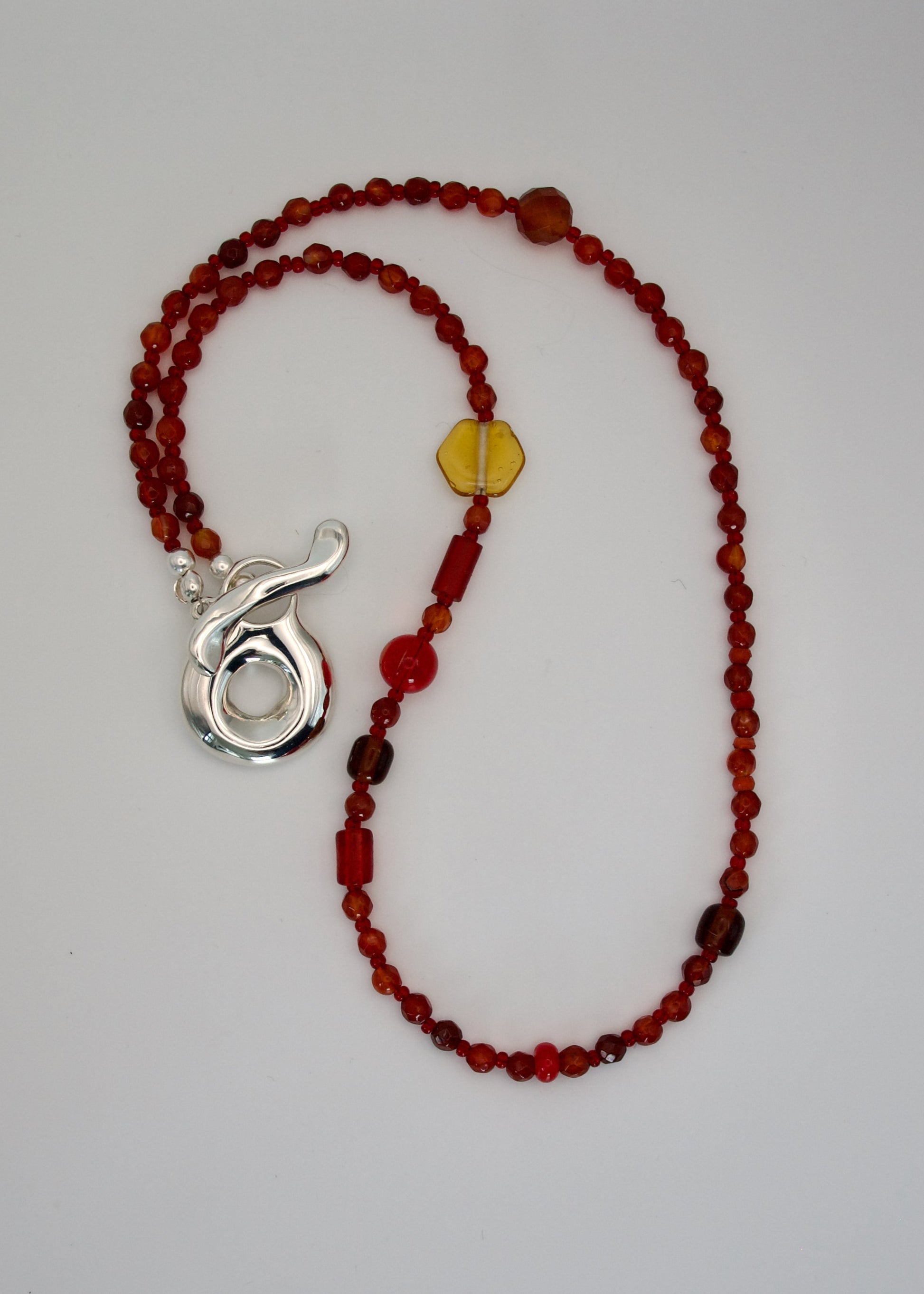 Necklace with red beads and a silver pendant on a light gray background
