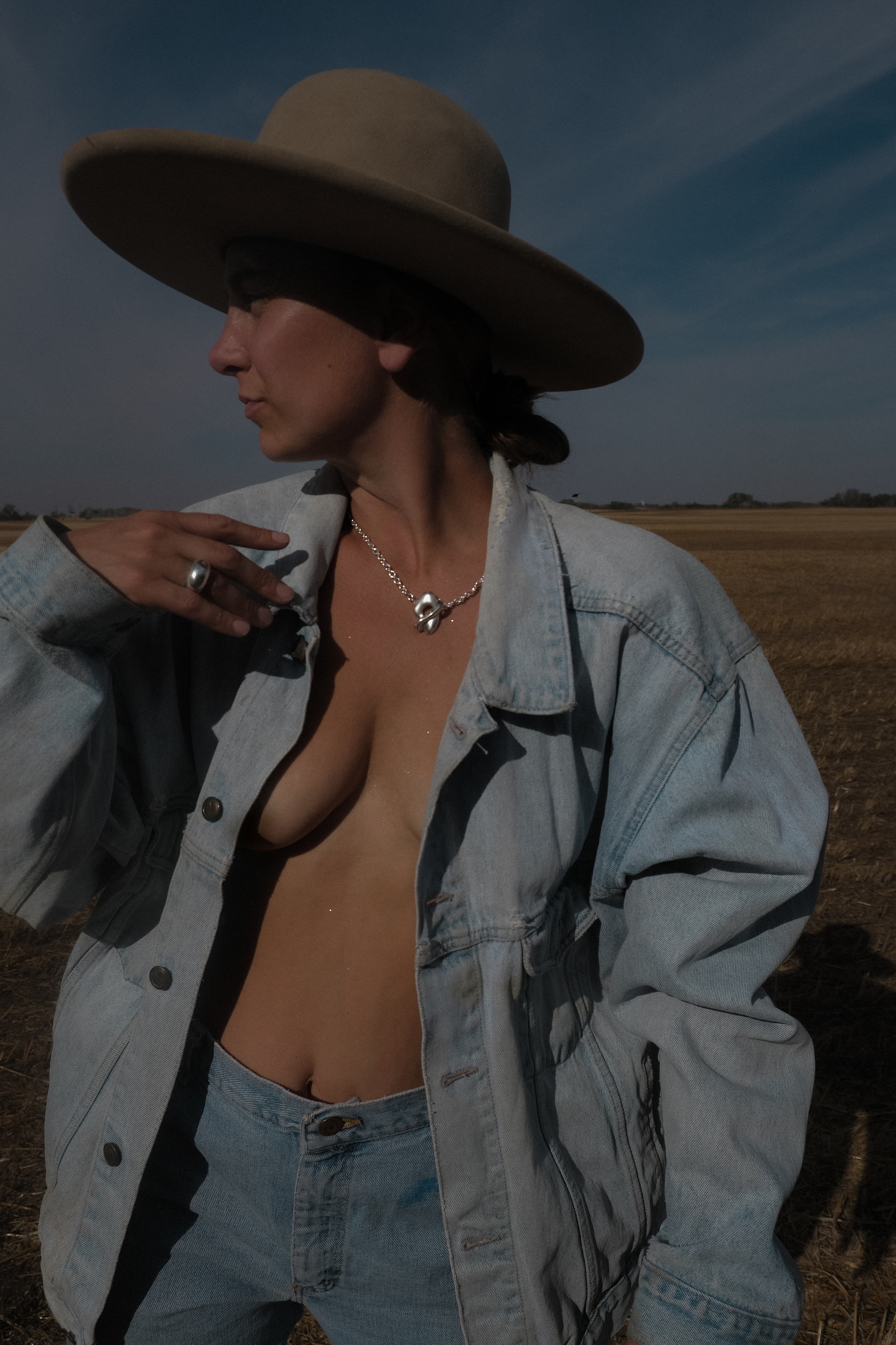 Person wearing a wide-brimmed hat and open denim jacket in a field wearing sculptured jewellleruy in sterling silver from SEOLA atelier