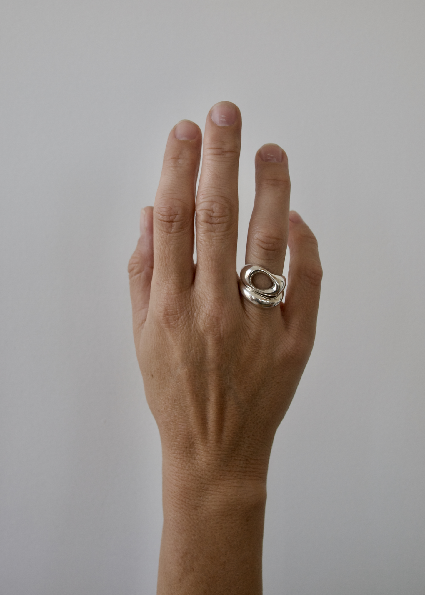 Hand wearing two stacking rings in sterling silver on a plain background