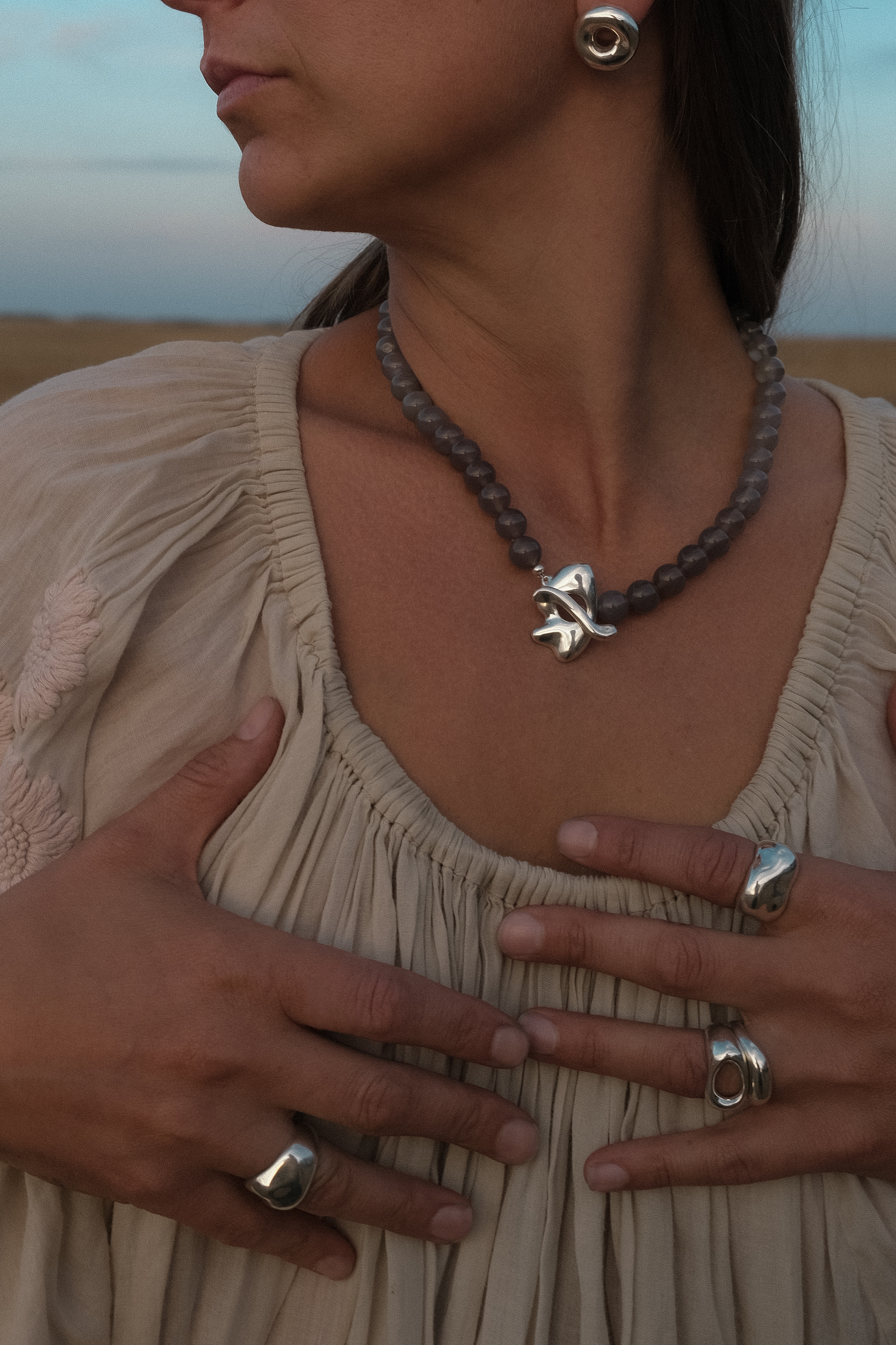 Woman wearing a necklace with a silver pendant and rings in sterling silver - sculptured and shiny, set against a desert landscape.