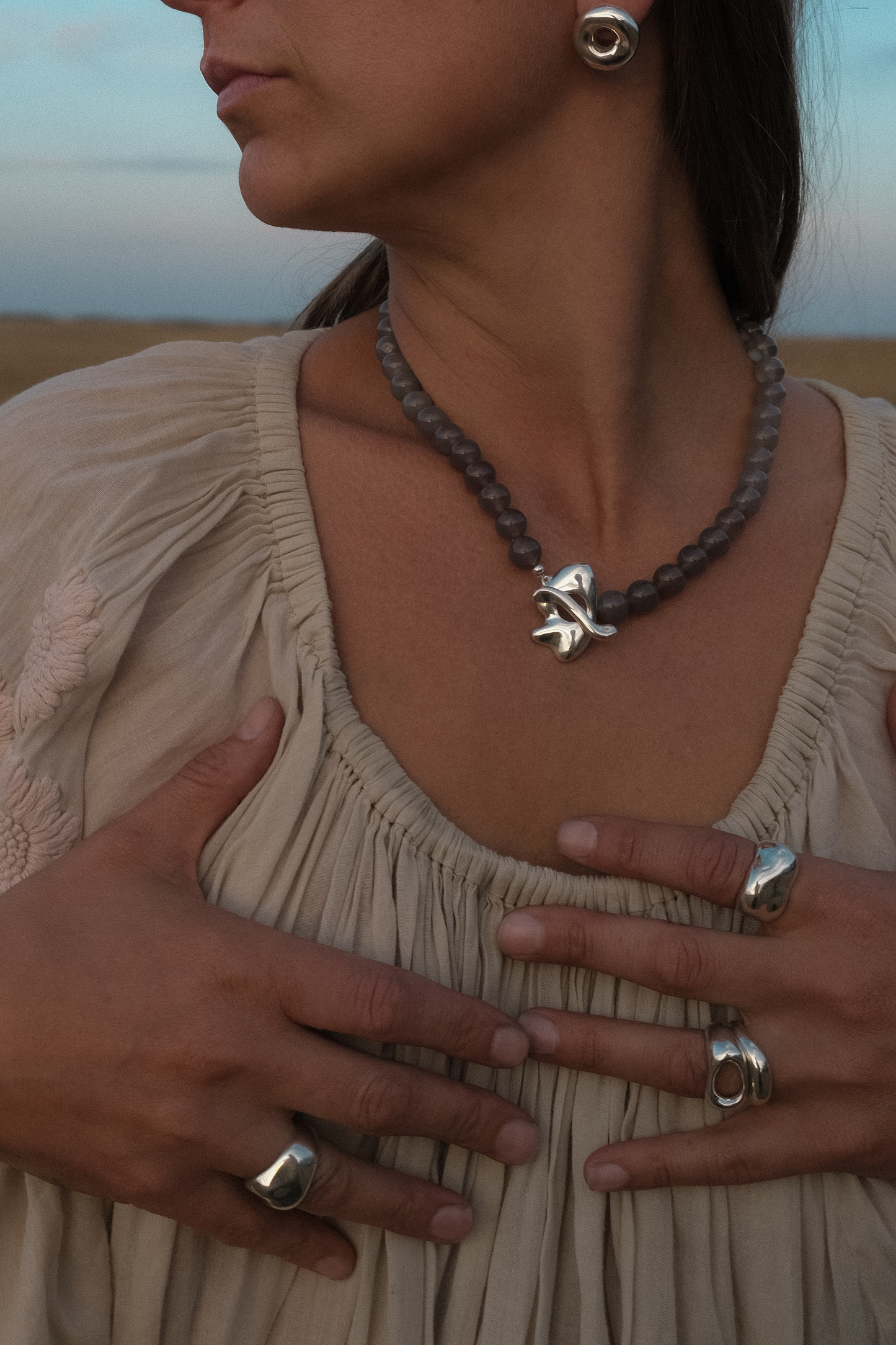 Woman wearing a necklace with a silver pendant and rings in sterling silver - sculptured and shiny, set against a desert landscape.