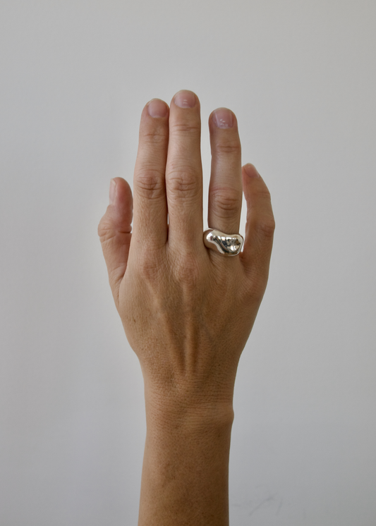 Hand wearing an organic smooth ssterling silver ring on a plain background