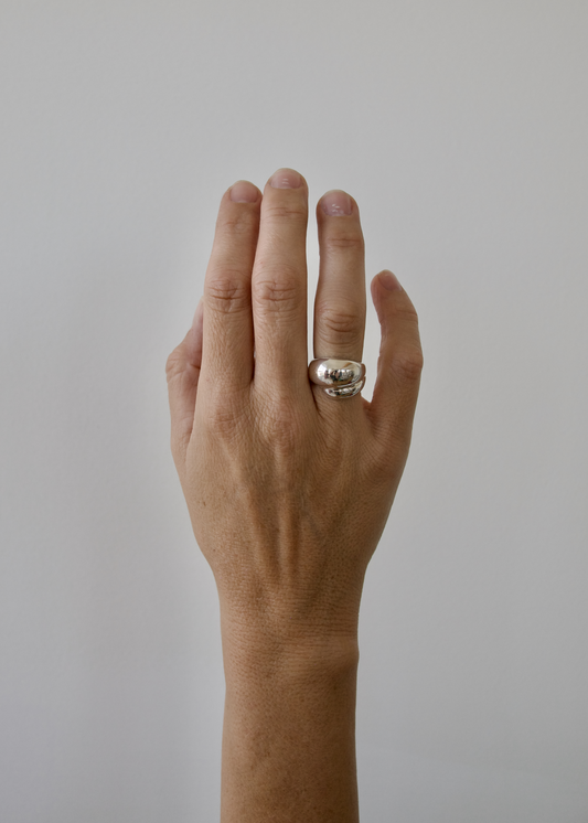 Hand wearing a oranic curled around silver ring on a plain background