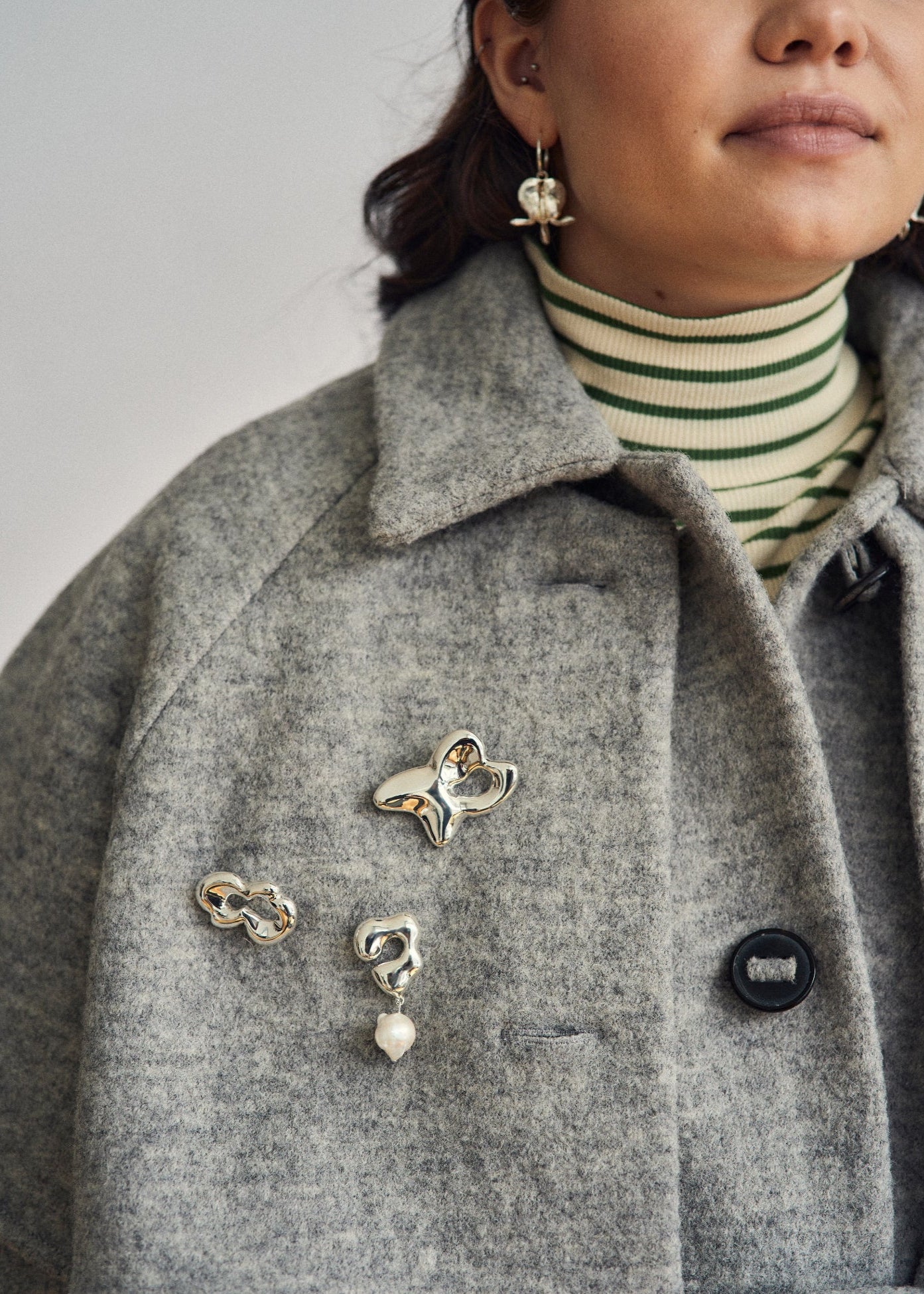 organic silver brooches styled on tailored grey coat, modern minimalist look
broches en argent aux lignes organiques portées sur un manteau– style minimaliste contemporain