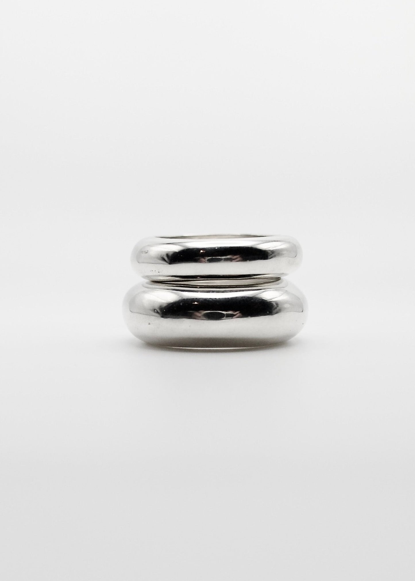 Jooni Ring displayed on a neutral background, highlighting its organic, round-shaped design and mirror-polished sterling silver finish. The jooni ring is on the top of the nilou ring to show the size difference and also their mirror shine together