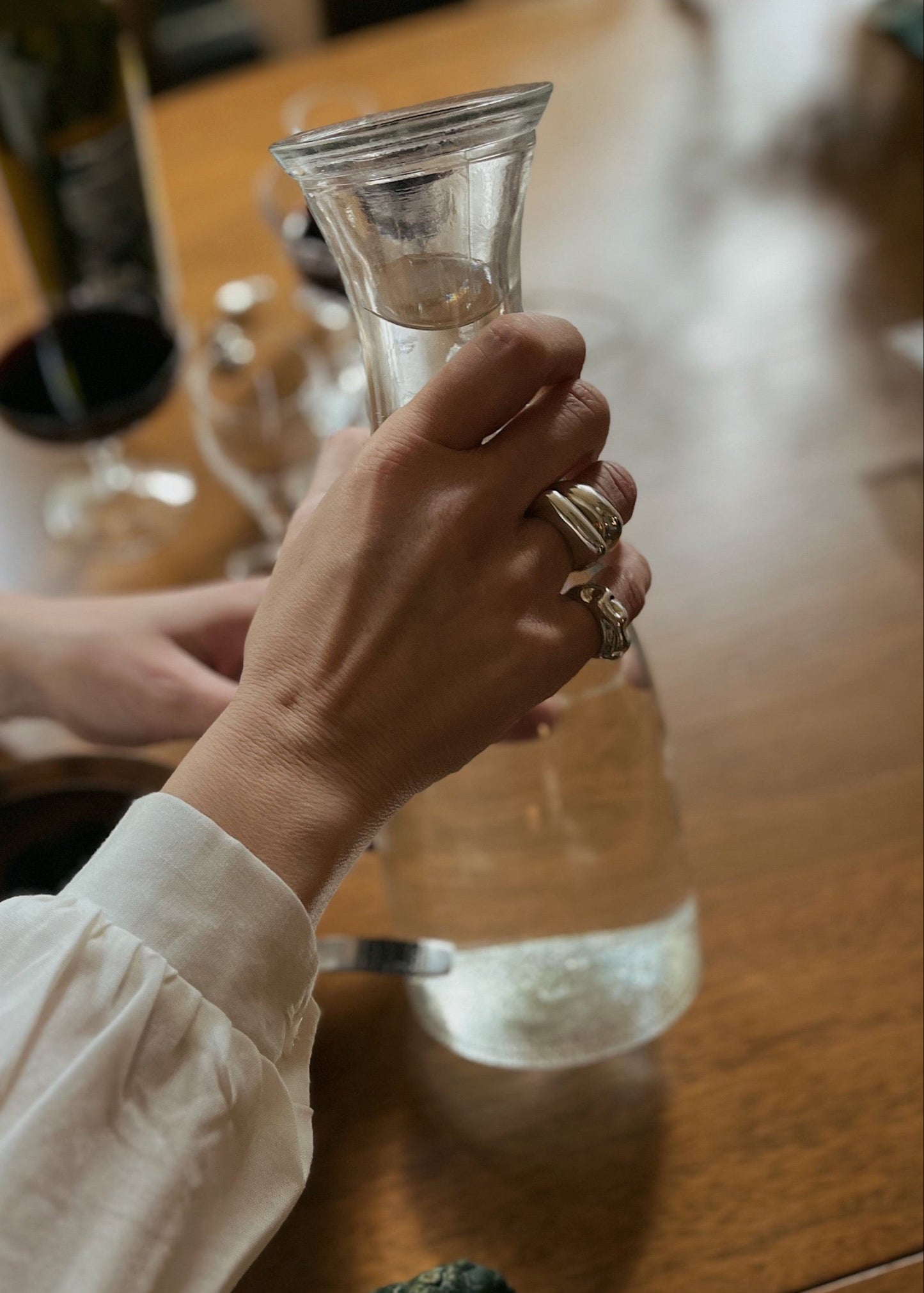 Model wearing the Astrid ring tacked with other rings while pouring water. Close-up of a model's finger wearing the Astrid Ring, emphasizing its elegant simplicity and comfortable fit.