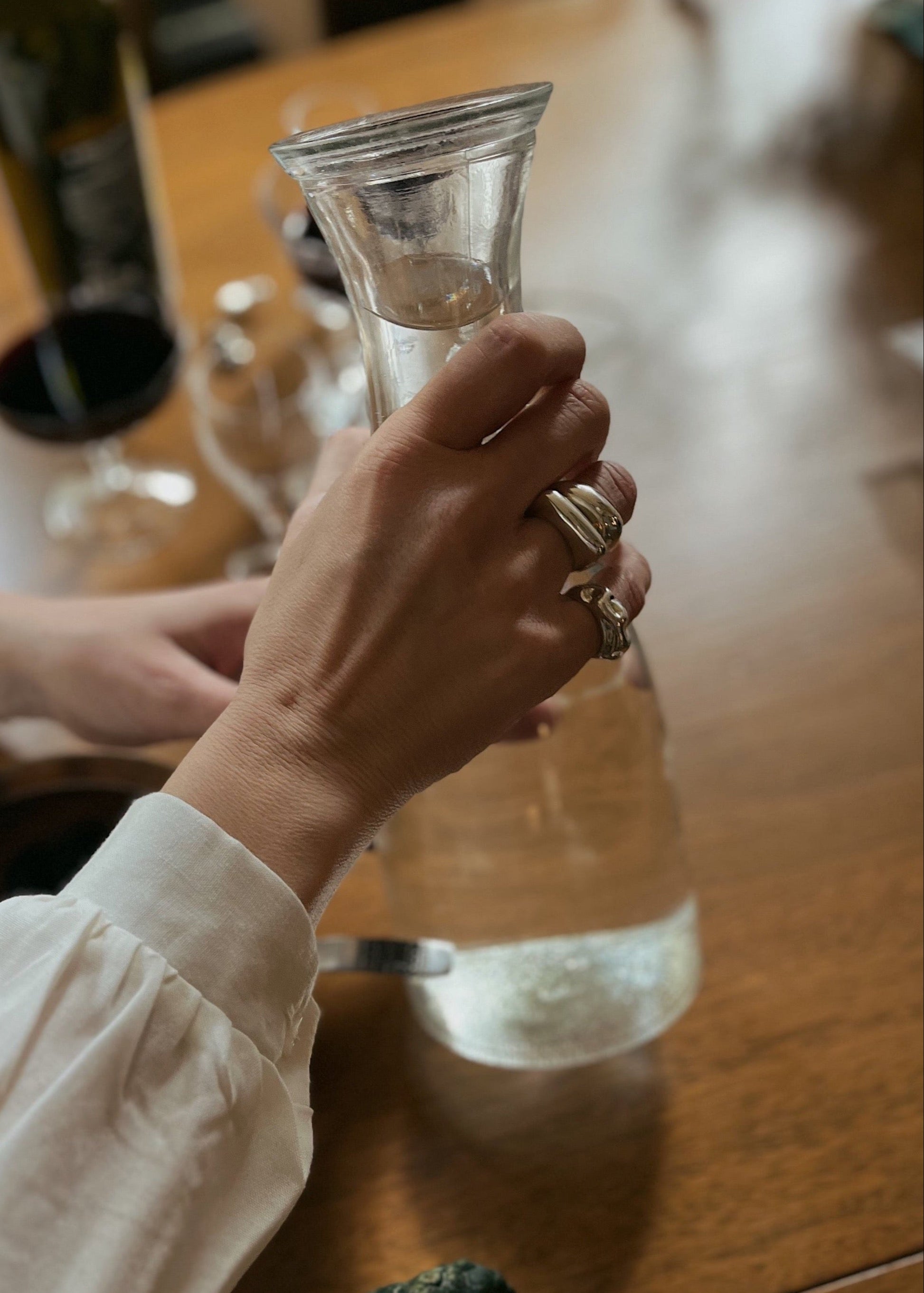 Model wearing the Astrid ring tacked with other rings while pouring water. Close-up of a model's finger wearing the Astrid Ring, emphasizing its elegant simplicity and comfortable fit.