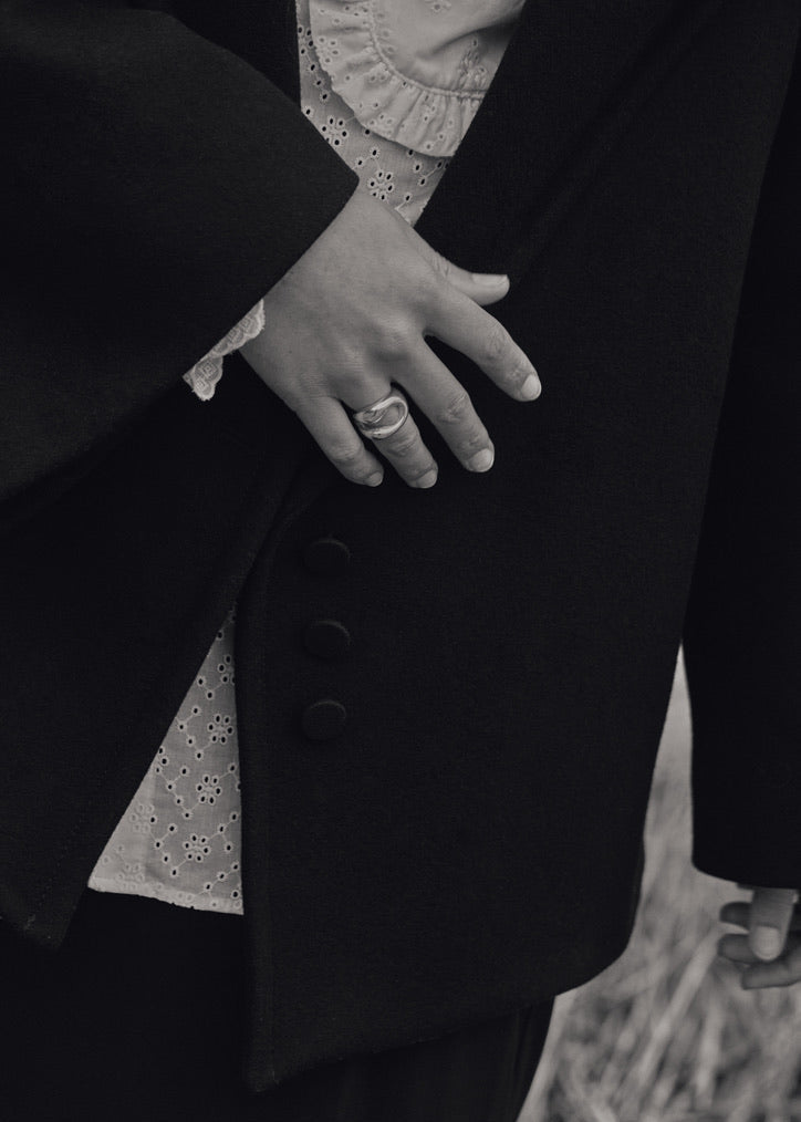 Close-up of a model's hand wearing the Eliza Ring, emphasising its unique design and comfortable fit. Model in black coat in black and white photo. 