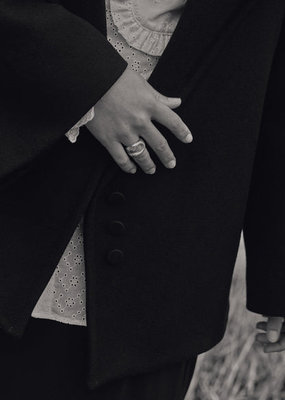 Close-up of a model's hand wearing the Eliza Ring, emphasising its unique design and comfortable fit. Model in black coat in black and white photo. 