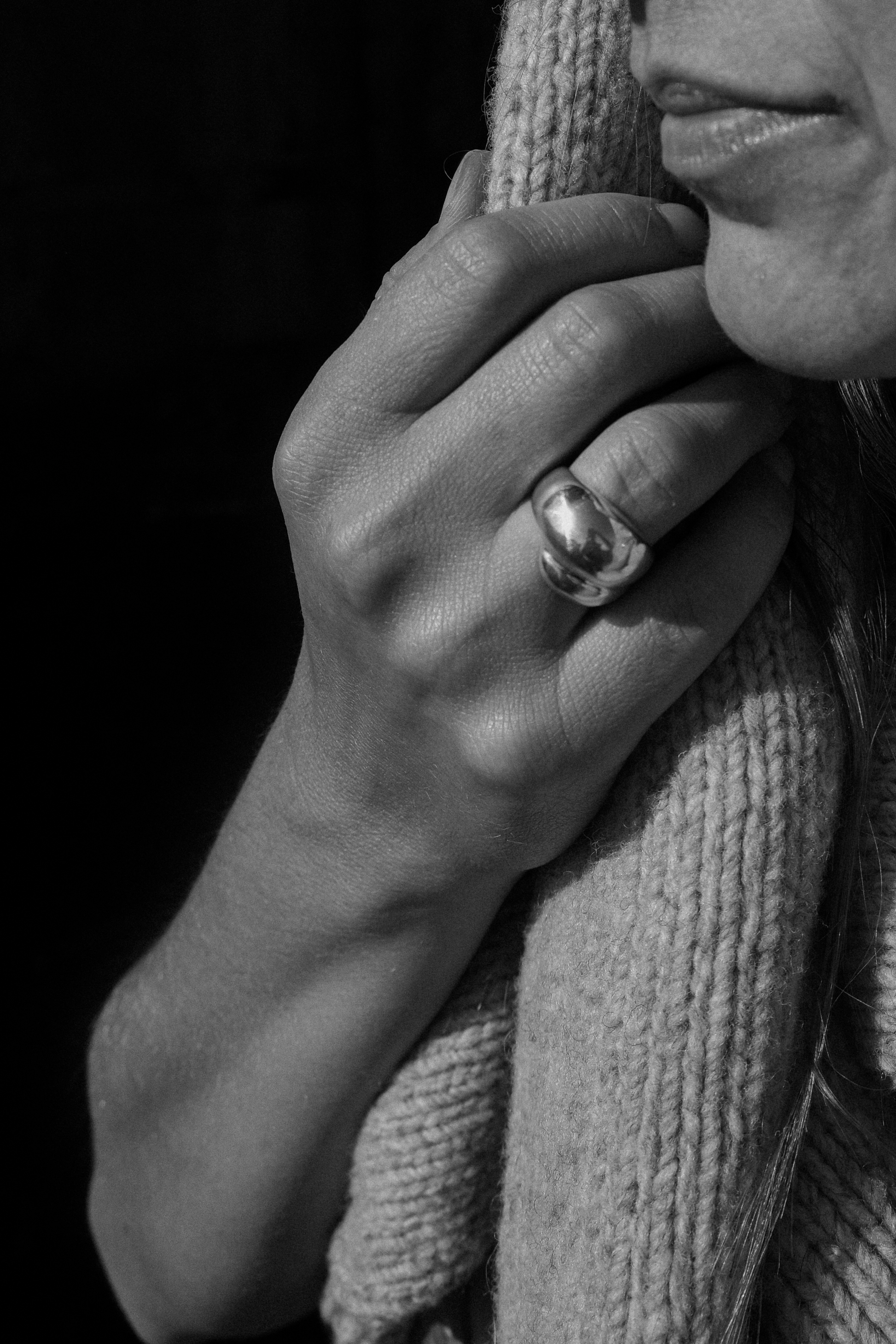 Close-up of a hand holding a knitted scarf with a dark background wearing a sculptured ring in sterling silver from SEOLA atelier 