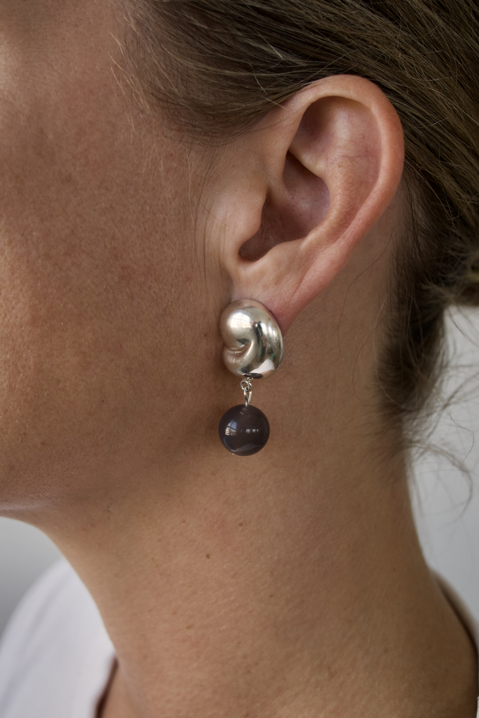 Close-up of an ear wearing a silver  sculptured ad organic earring with a dark  grey agate bead.