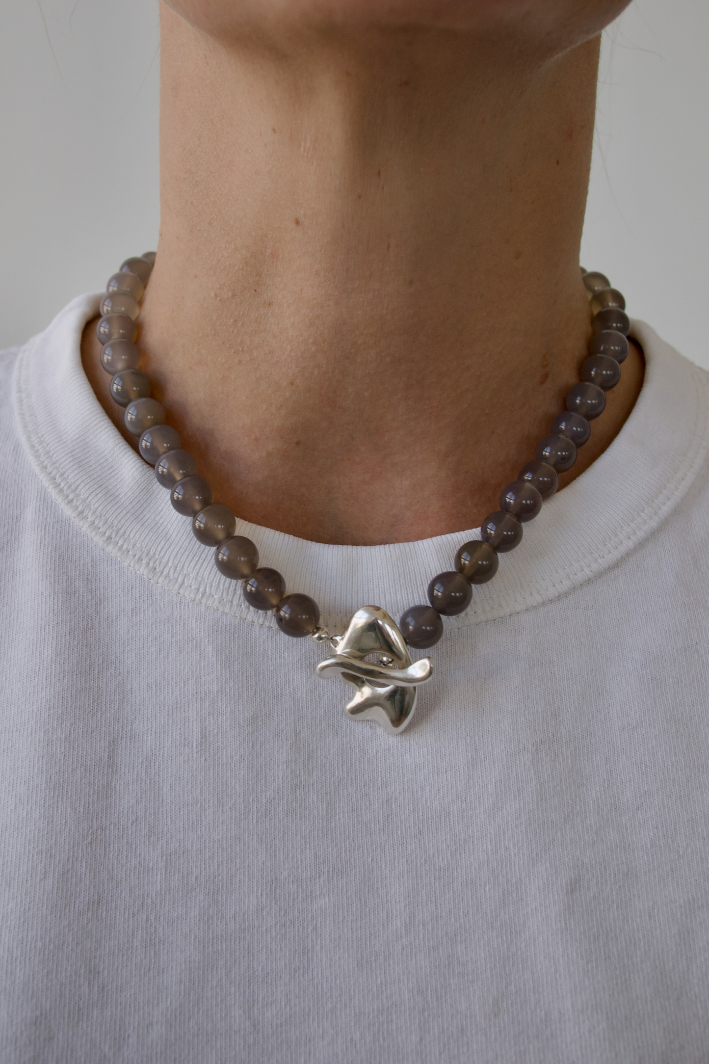 Necklace with grey beads and a silver star-shaped pendant worn by a person on a plain background