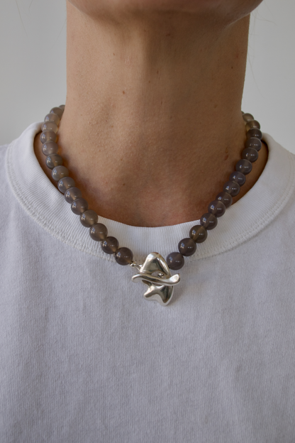 Necklace with grey beads and a silver star-shaped pendant worn by a person on a plain background