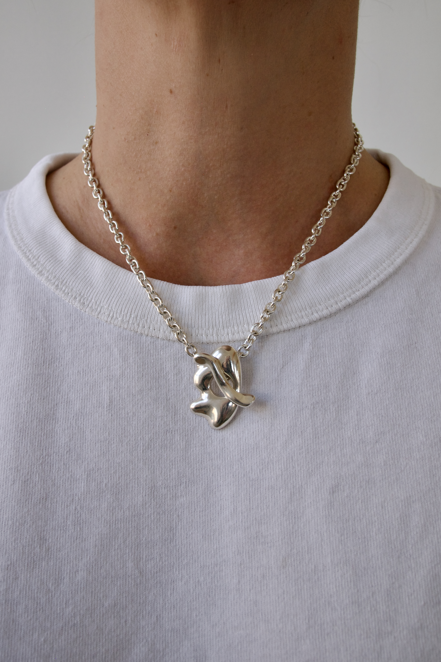Person wearing a silver necklace with a leaf pendant on a plain background