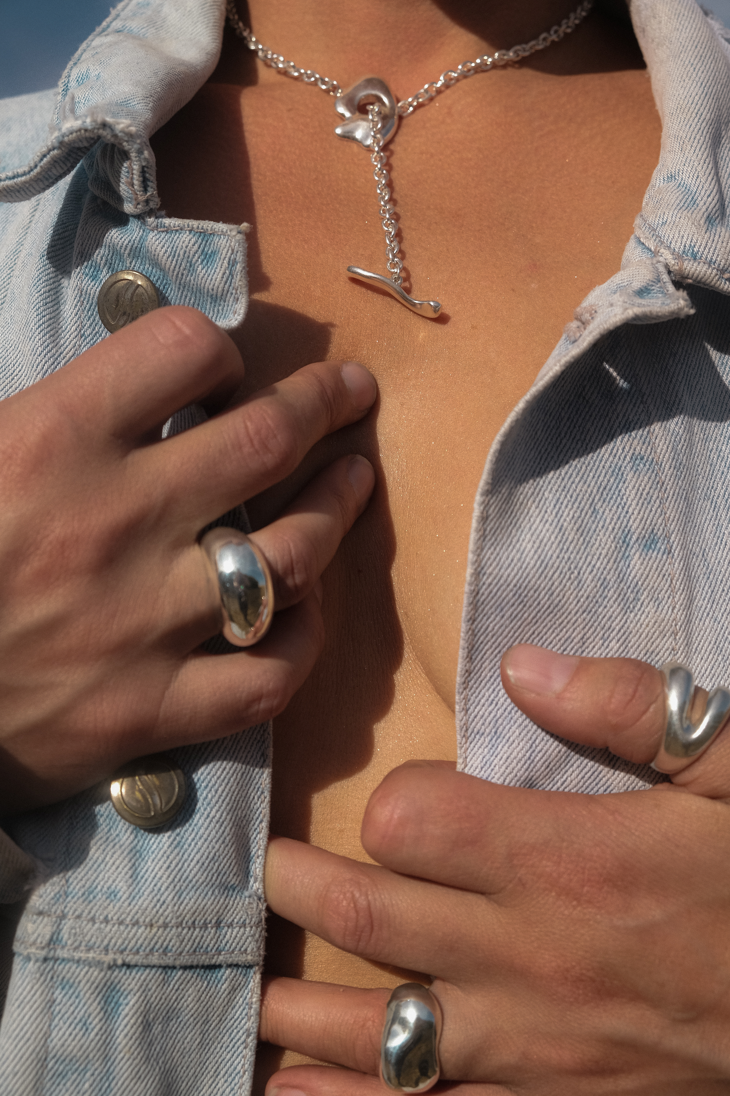 Close-up of a person wearing silver rings and a necklace with a blue denim jacket.