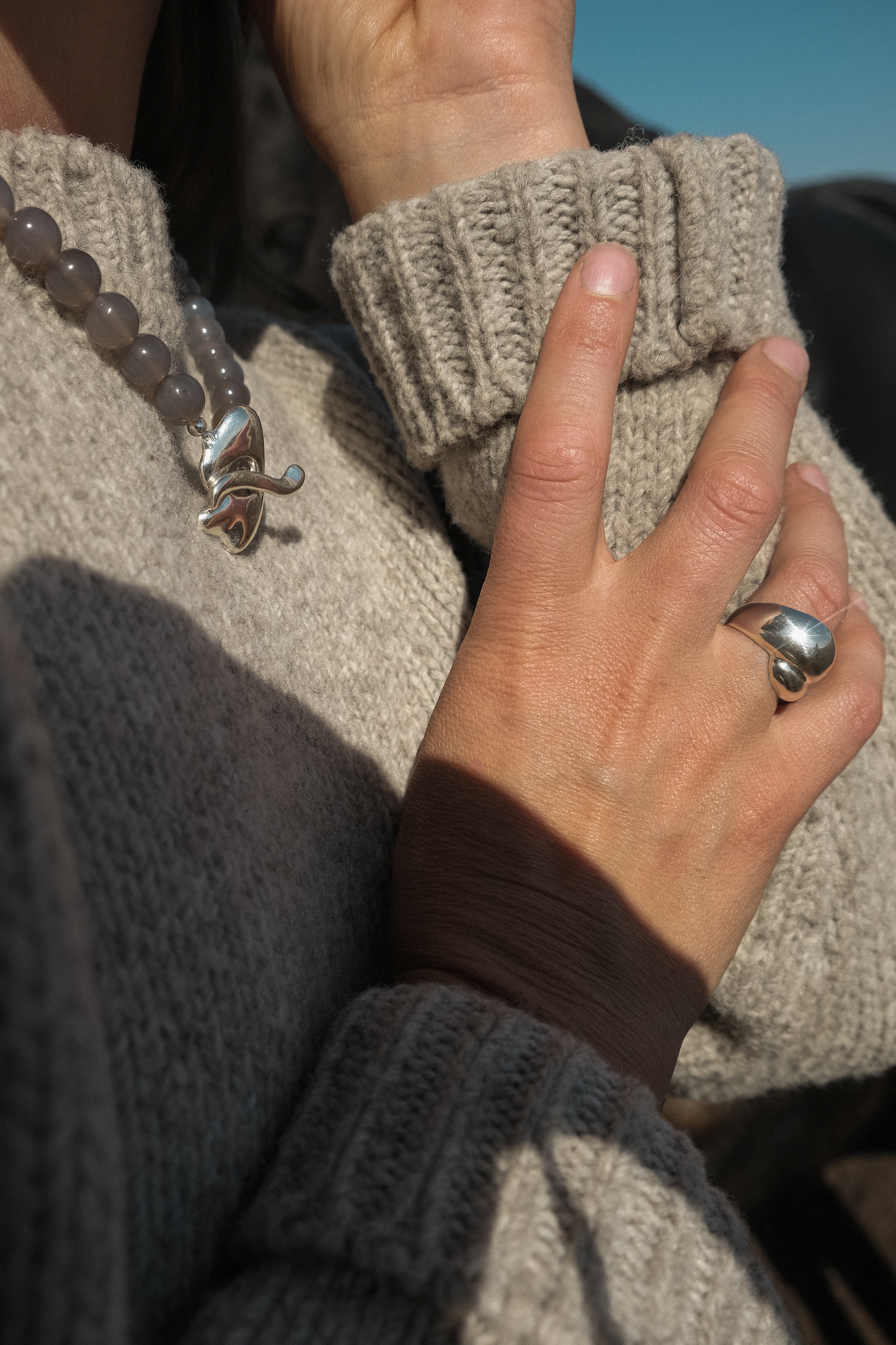 Close-up of a person wearing a textured sweater with a hand gesture against a blurred background and silver jewellery in sterling silver, statement pieces organci and sculptured