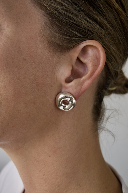 Close-up of a person wearing a silver organic spiral earring against a neutral background